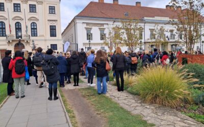 A képen a szociális ágazati dolgozók kicsit kevesebb mint egy évvel ezelőtti tüntetése látható, még a Fidesz-kormányzat alatti Miniszterelnöki Kabinetiroda, a Karmelita kolostor hírhedt épülete előtt 2025 szeptemberéből.
